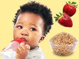 A baby drinks from a bottle beside strawberries and a bowl of cereal.