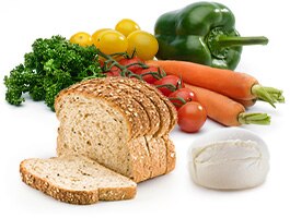 A pile of wheat bread, tomatoes, cheese, carrots, kale and a bell pepper.