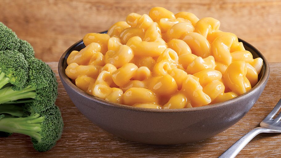 A bowl of Stouffer's macaroni and cheese on a table with a fork and bunches of broccoli.