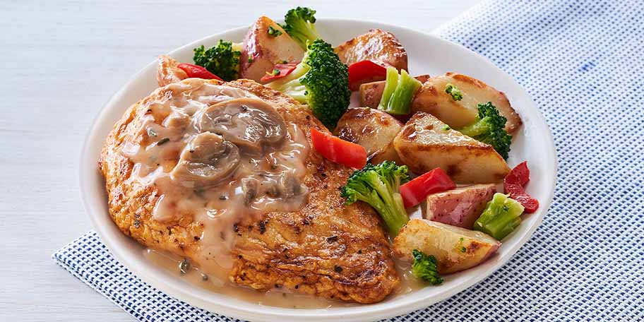 Un plato de pollo asado a las hierbas con papas, brócoli y hongos sobre una servilleta de tela.