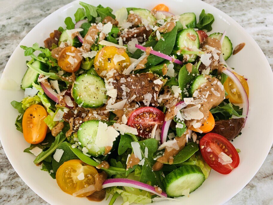 Un plato blanco lleno de ensalada con pepinos, tomates, cebollas, queso y bistec portobello.