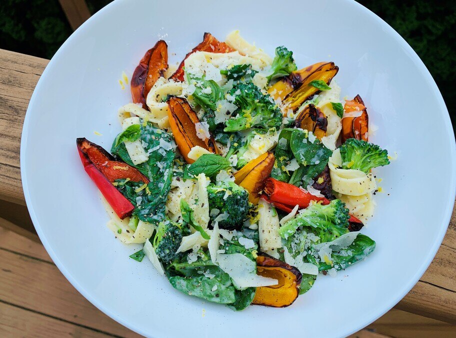 Un plato blanco de fettuccine alfredo vegetariano con espinacas, brócoli, pimientos y queso.