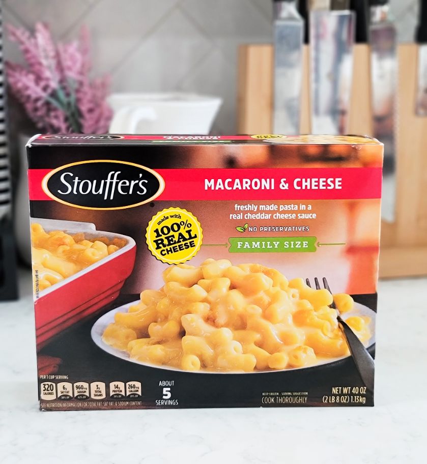 Una caja de Stouffer’s Macaroni & Cheese tamaño familiar sobre el mostrador de una cocina frente a una planta y un bloque de cuchillos.