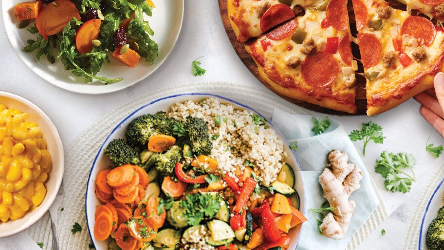 A DiGiorno pizza on a wooden tray near cherry tomatoes, a red pepper and basil on a granite counter.
