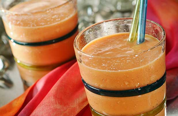 Two orange smoothies in glasses with straws beside an orange napkin.