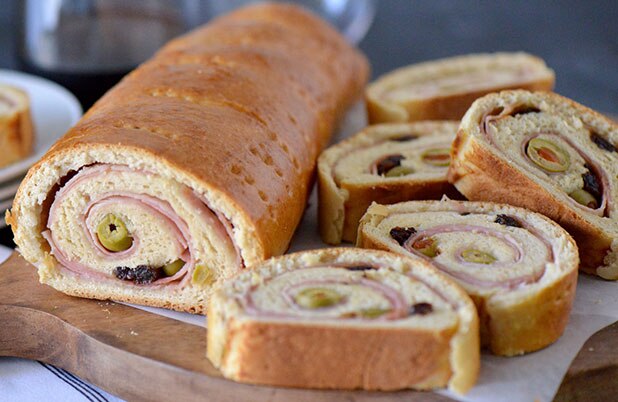 Una hogaza de pan de jamón venezolano junto a lonchas rellenas de jamón y aceitunas verdes.