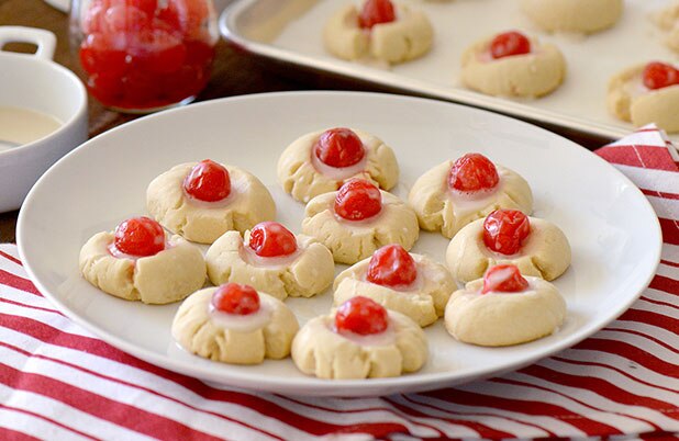 Un plato de galletas de mantequilla de almendras cubiertas con cerezas y glaseado.