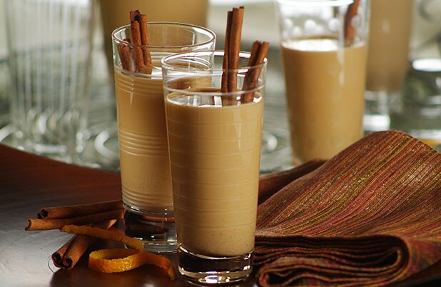Vasos de Cola de Mono chilena con ramitas de canela al lado de un mantel de tela doblado.