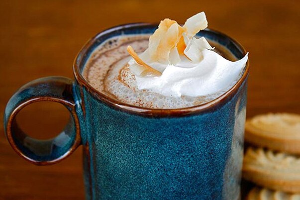 Una taza azul de cerámica con chocolate caliente, decorada con naranja y crema batida.