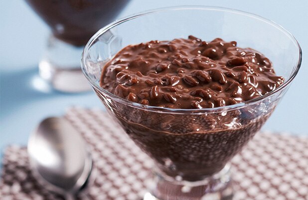 Un plato transparente de arroz con leche de chocolate junto a una cuchara.