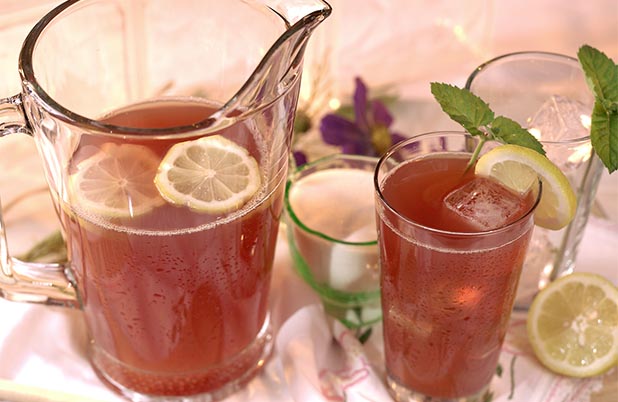Una jarra y un vaso llenos de limonada con moras, hielo, rebanadas de limón y adorno de menta. 