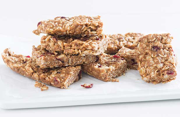 Barras de cereales con frutas deshidratadas y granos apiladas sobre un plato blanco.