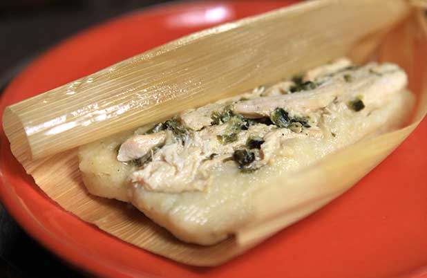 Un tamal de pollo y poblanos abierto sobre un plato naranja.