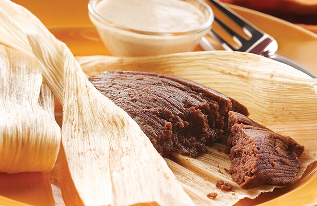 Un tamal de chocolate abierto sobre un plato naranja con un tenedor y una salsa cremosa.