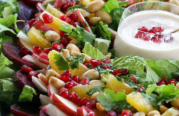 Una ensalada de Nochebuena llena de semillas de granada y rodajas de manzana alrededor de una taza de aderezo.