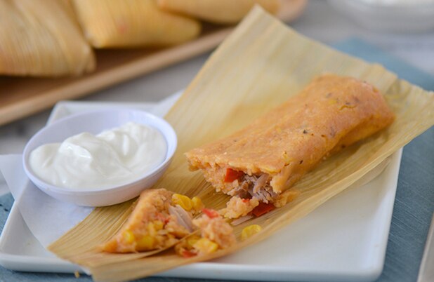 Un tamal estilo cubano abierto con maíz, cerdo y chile sobre un plato con crema agria.