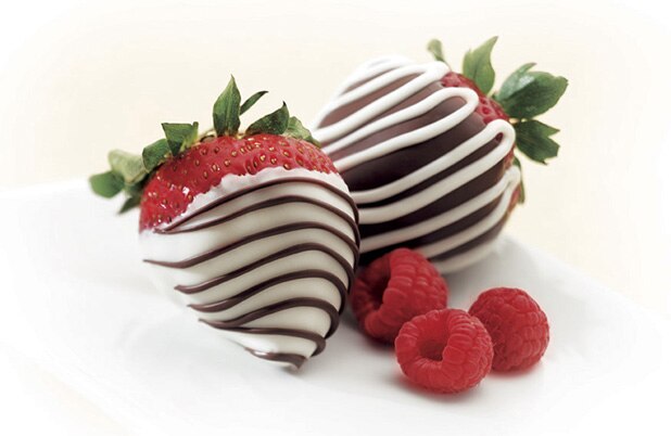 Fresas cubiertas con chocolate blanco y oscuro sobre una servilleta de tela con frambuesas frescas.