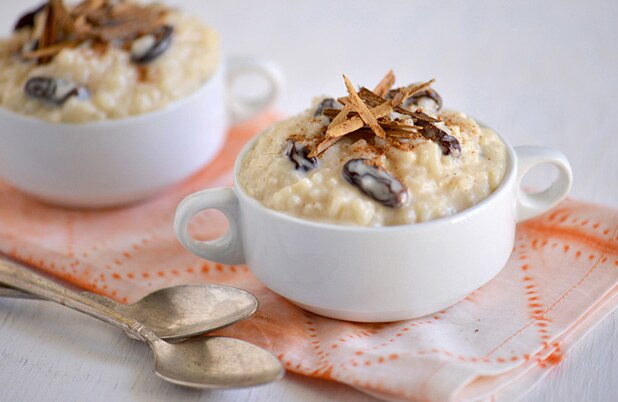 Dos platos de cerámica llenos de arroz con leche estilo dominicano cubierto con pasas y ramitas de canela.