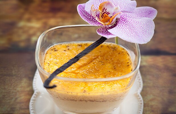 Un plato transparente con flan de vainilla y guarnición de vainilla.