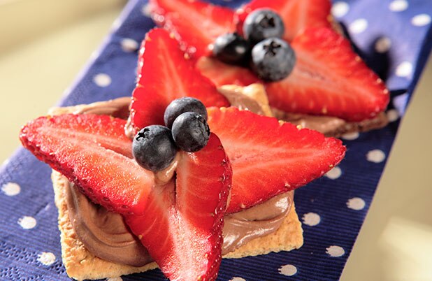Galletas Graham cubiertas con chocolate y fresas y moras azules frescas sobre una servilleta de tela.