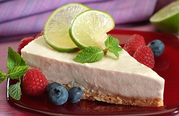 Una porción de tarta de lima adornada con menta sobre un plato con bayas frescas.