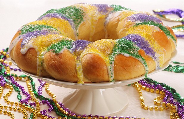 Una Rosca de reyes de Mardi Gras con glaseado y azúcar color púrpura, verde y amarillo espolvoreada encima y rodeada por cuentas de Mardi Gras.