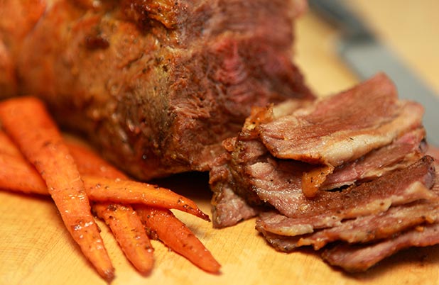 Rodajas de cerdo asado con zanahorias asadas sobre una tabla para cortar.