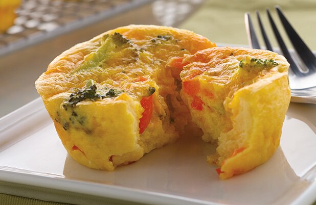 Un mini quiche con brócoli y queso cheddar cortado sobre un plato con un tenedor.