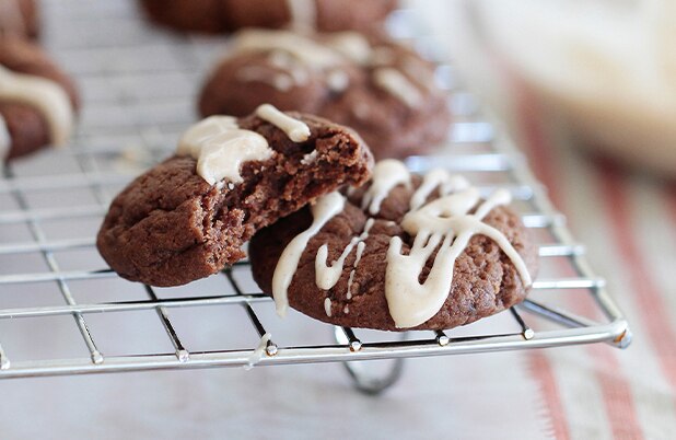 Dos galletitas de chocolate con baño blanco por encima enfriándose sobre una rejilla.