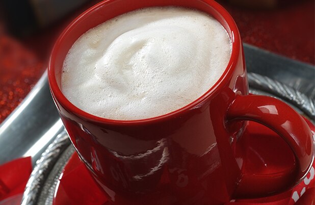 Una taza roja llena de espuma sobre un platillo plateado y una servilleta roja.