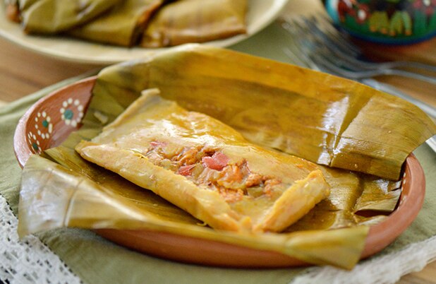 Un tamal puertorriqueño abierto relleno con cerdo, chiles y aceitunas sobre un plato de cerámica.