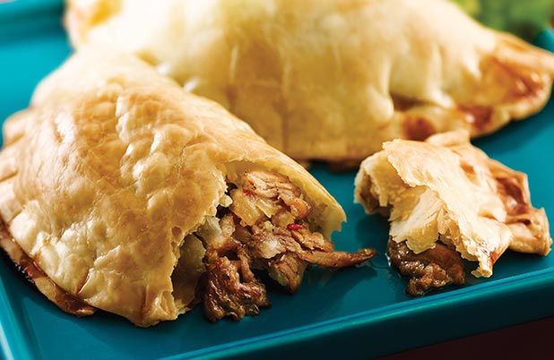 Empanadas hojaldradas con carne deshebrada sobre un plato azul.