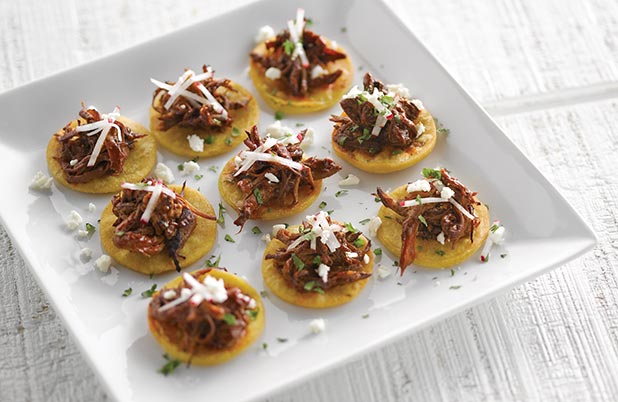 Un plato de tartaletas de tamal hechas de masa de maíz y cubiertas con carne de cerdo, cilantro y queso.