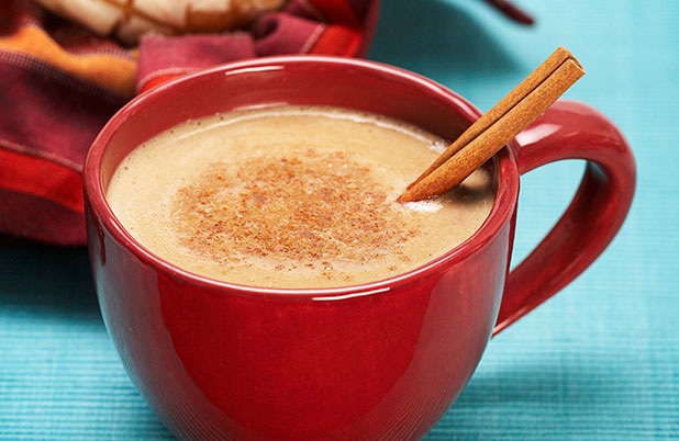 Una taza roja llena de chocolate caliente y una rama de canela sobre un mantel blanco.