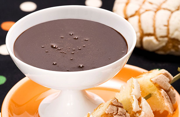 Un plato blanco de fondue de chocolate junto a brochetas de pan dulce.