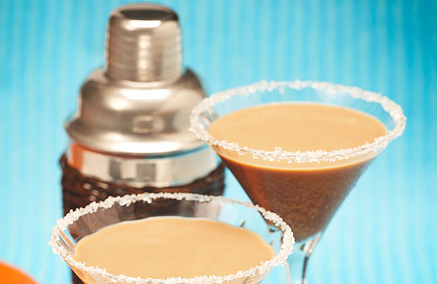 Martinis de café en vasos con borde de azúcar delante de una coctelera.