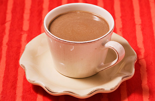 Una taza blanca llena de atole de chocolate y calabaza sobre un mantel naranja.