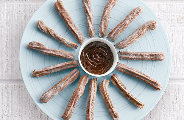 Una taza de salsa ABUELITA rodeada de churros en un plato.