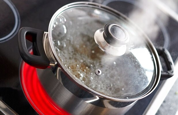 Agua hierve en una olla con tapa y el vapor se eleva de ella.