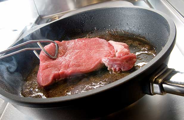 Un trozo de bistec se sella en una sartén.