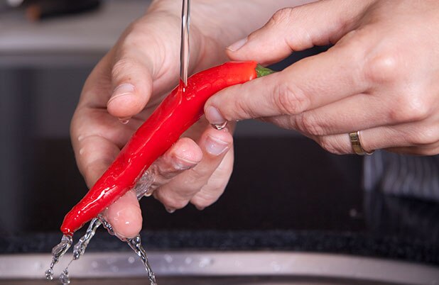 Manos enjuagan un pimiento rojo.