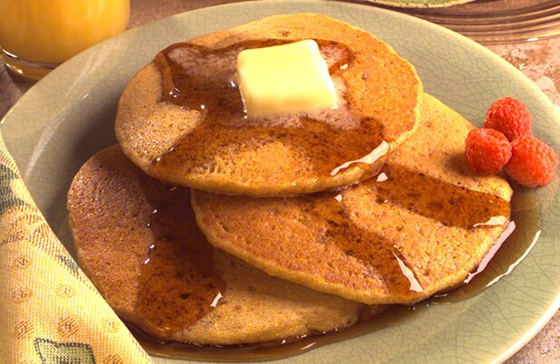 Un plato de panqueques con mantequilla, jarabe y frambuesas frescas.