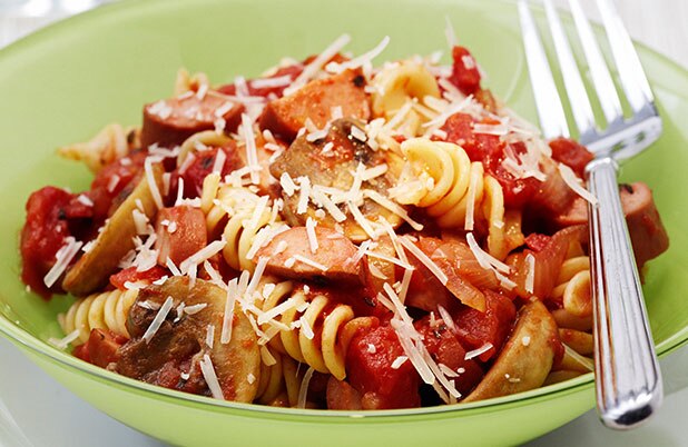 Un tazón color verde de pasta rizada con salsa y queso parmesano junto a un tenedor.