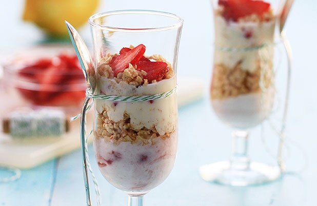 Una copa de champaña con una cuchara atada a la misma y rellena con parfait de yogur de fresa y granola.
