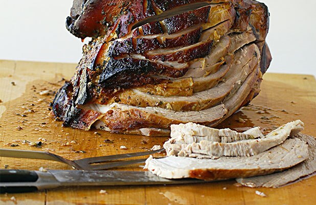 Pavo rebanado sobre una tabla para cortar junto a un tenedor y cuchillo de trinchar.