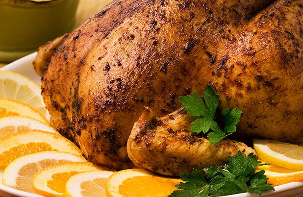 Un pavo entero en una bandeja rodeado de rebanadas de naranja.