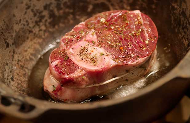 Un trozo de bistec en una sartén con especies y hierbas de olor.