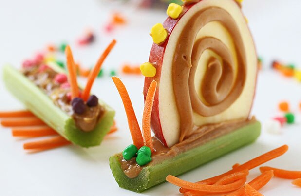 Palitos de apio decorados como caracoles con crema de cacahuate (mantequilla de maní), zanahorias, rebanadas de manzana y mini dulces.
