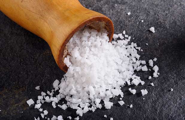 Un montoncito de sal de un salero sobre una superficie color negro.