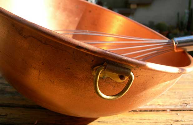 Un batidor reposa sobre un lado de un tazón de cobre.